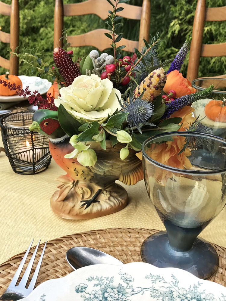 A sweet little bird perches on a ceramic squash flanked by a pair antique clawfoot candlesticks.