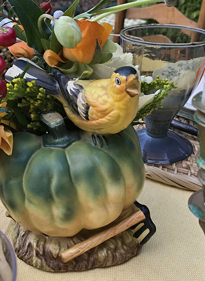 A sweet little bird perches on a ceramic squash flanked by a pair antique clawfoot candlesticks.